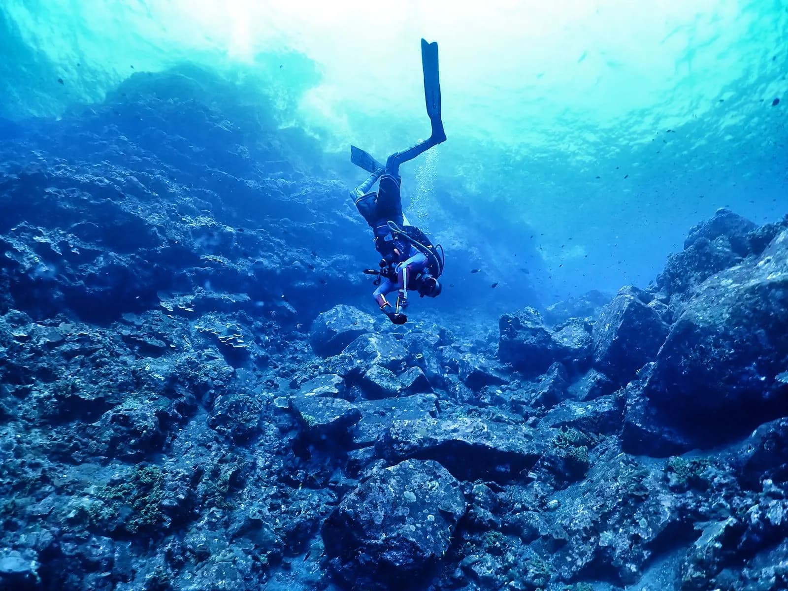 Diver descending head-down toward a rocky deep seabed in clear blue Andaman water