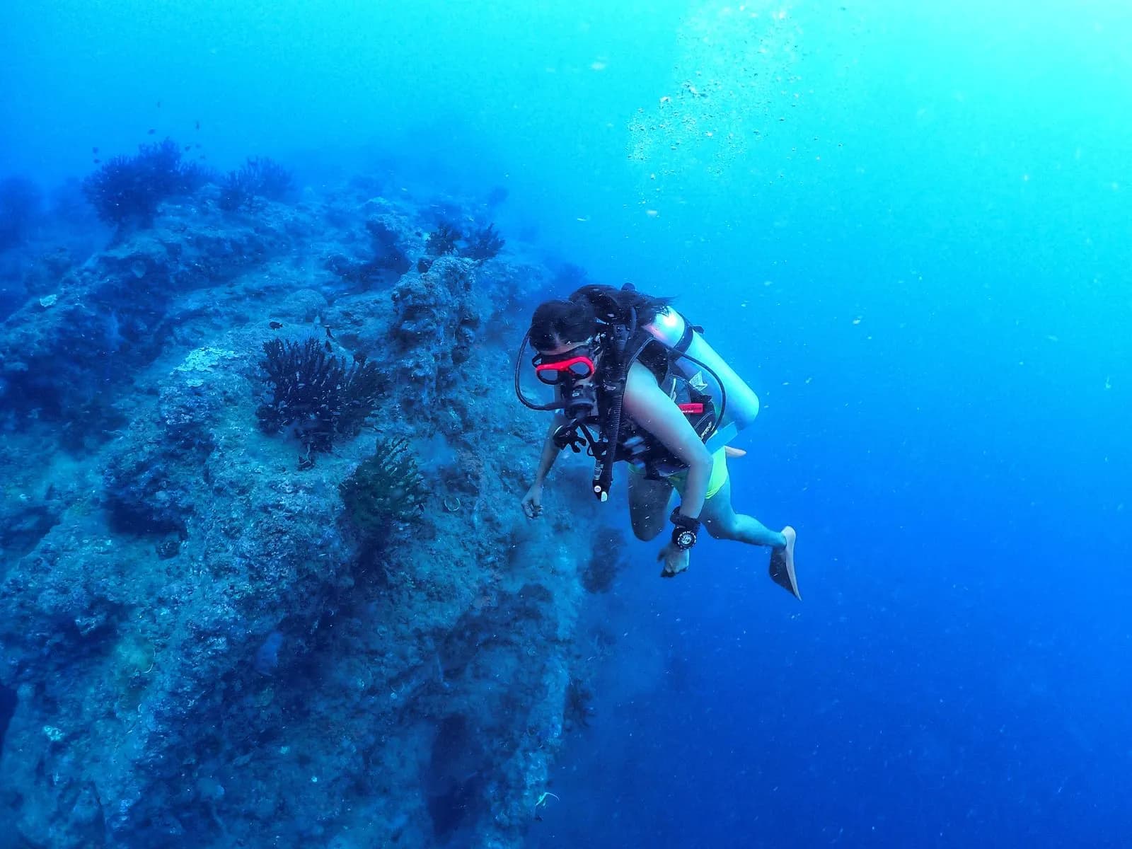 Diver with red mask frame exploring a steep reef wall in deep blue water