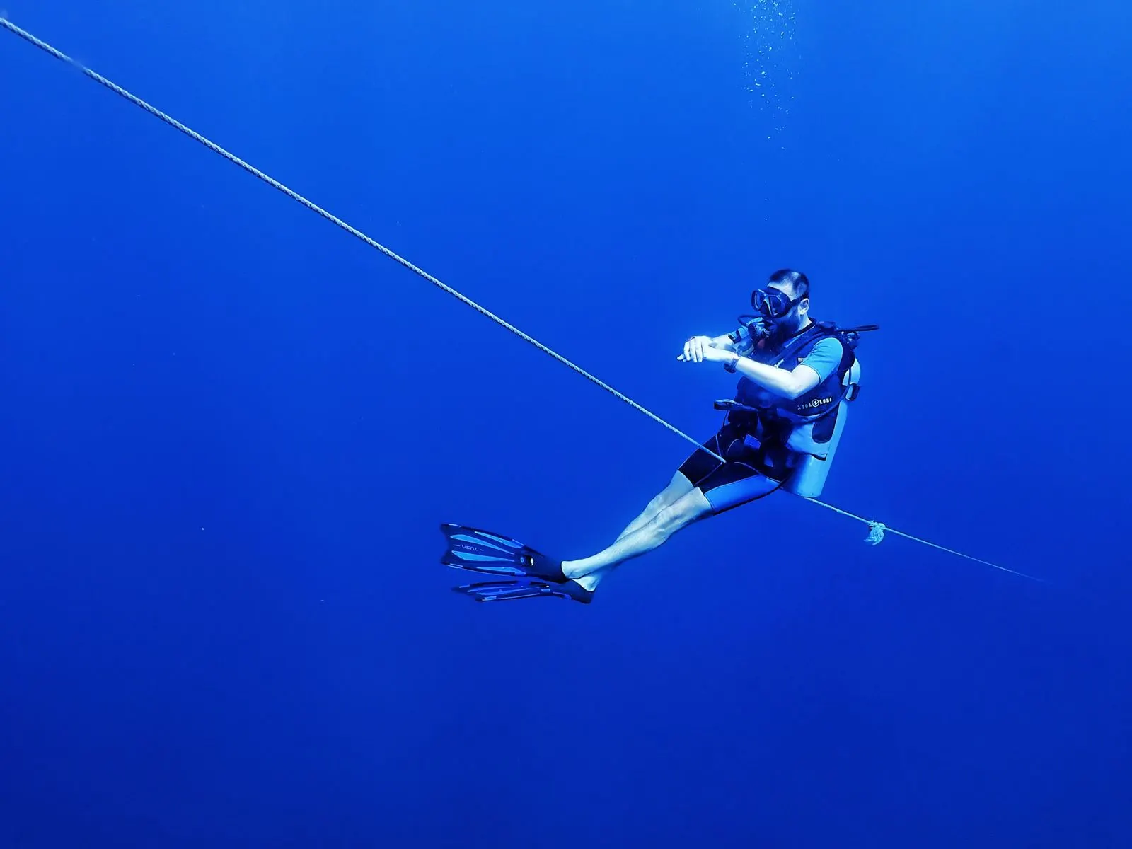 Diver floating neutrally beside a mooring line in deep blue open water — SSI Specialty Perfect Buoyancy