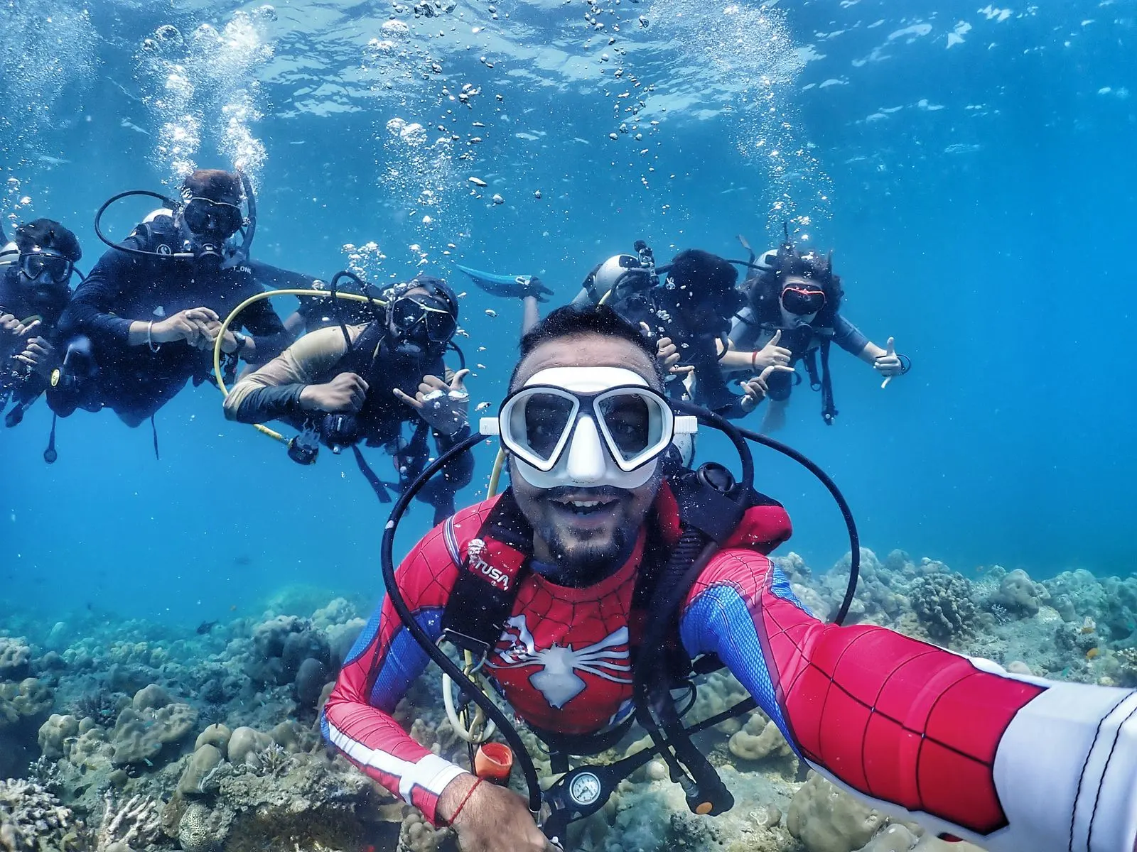 Oceanspidey in a Spider-Man wetsuit taking an underwater group selfie with divers over a Havelock reef